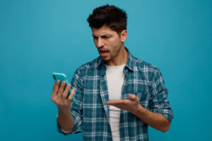 aggressive young man holding looking mobile phone showing empty hand isolated blue background